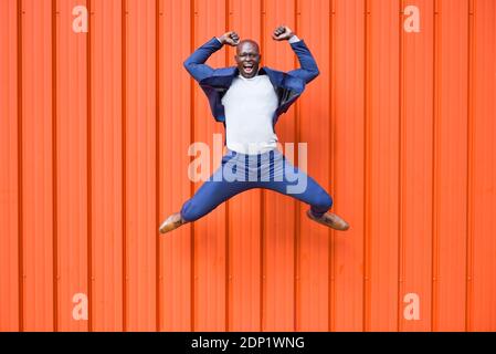 Successfull businessman jumping in the air in front of orange wall screaming Stock Photo