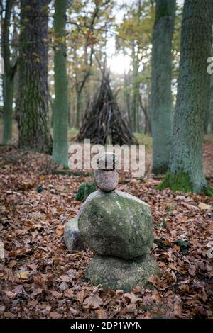Mystical shot of a stone cairn in the woods with a wooden stack of branches in the background Stock Photo