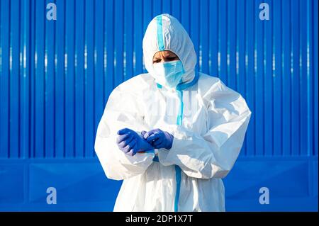 Female nurse wearing glove while standing against blue wall on sunny day Stock Photo