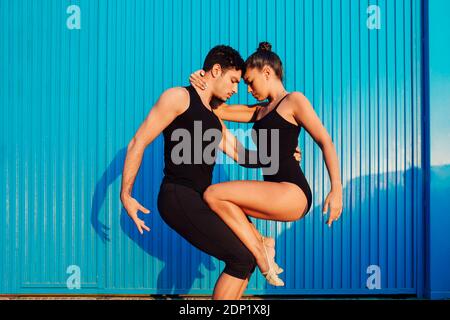 Male and female professional gymnasts doing balancing pose by blue corrugated metal Stock Photo