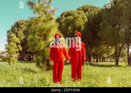 Young couple wearing red overalls and hats standing hand in hand on a meadow looking at each other Stock Photo