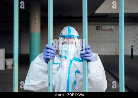 Female nurse standing inside parking garage while wearing protective suit looking through bars Stock Photo