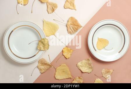 Two ceramic plates and fallen leaves on a beige brown background. Autumn breakfast. Top view. Stock Photo