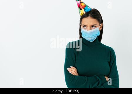 Sad young woman in medical mask and festive cap on white background Stock Photo