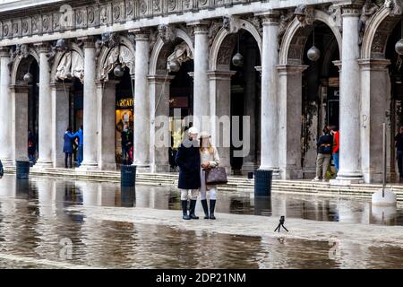 A Young Couple Take A Selfie During Acqua Alta (High Tide) St Mark’s Square, Venice, Italy. Stock Photo