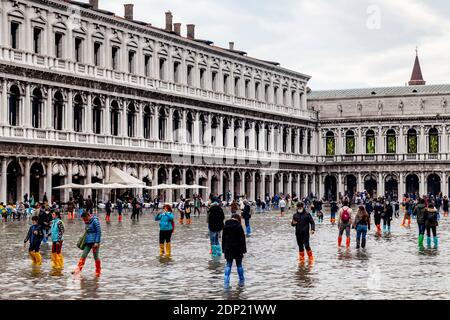 Visitors Wearing Water Protective Plastic Shoe Covers In St Mark’s Square During Acqua Alta (High Tide), Venice, Italy. Stock Photo