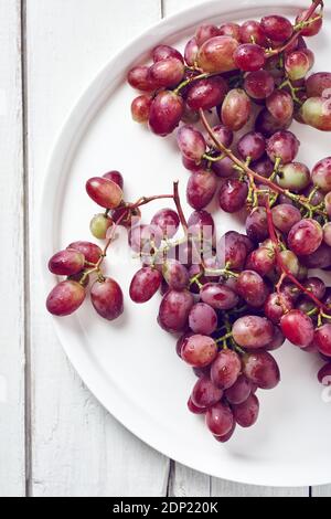 Ripe red grapes in a plate on a white wooden background. Top view. Stock Photo