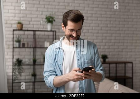 Hopeful young male standing indoors involved in dialing phone number Stock Photo