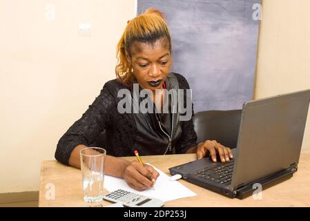 pretty businesswoman sitting at desk taking notes and working in front of a laptop Stock Photo