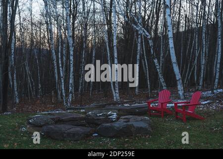 Two red chairs next to a bon fire in front of birch trees Stock Photo