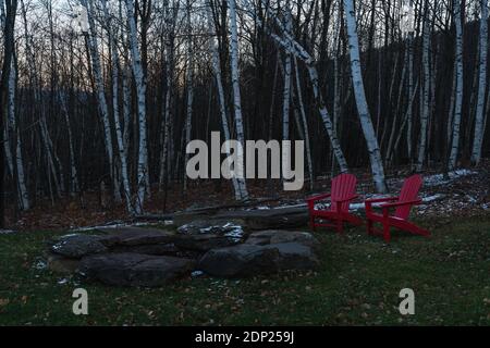 Two red chairs next to a bon fire in front of birch trees Stock Photo