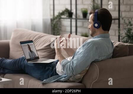 Positive man reclining on couch talking with friend via videoconference Stock Photo