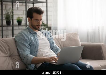 Confident young man sitting on sofa at home using laptop Stock Photo