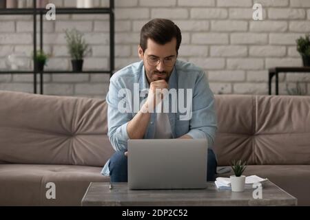Pensive young male working at home focused on computer screen Stock Photo