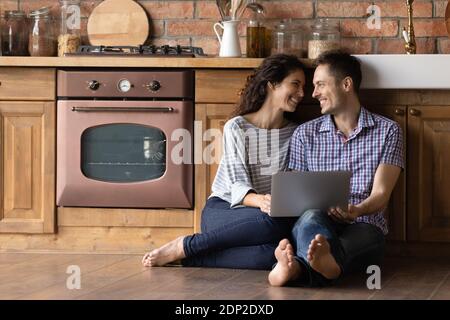Loving couple sitting on kitchen floor planning wedding using laptop Stock Photo