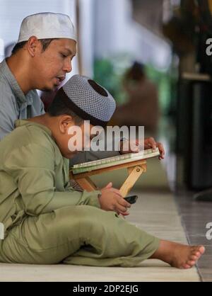 Father and Son after Friday Prayers at Masjid Al-Islah, Al-Islah Mosque, Singapore.  Father Reading, Son Using Cell Phone. Stock Photo