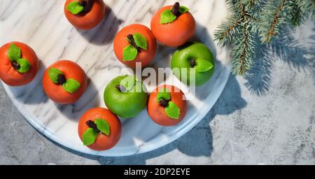 Marzipan sponge apples, green and red. Panoramic flat lay on marble board with fir twigs, winter decorations. Stock Photo