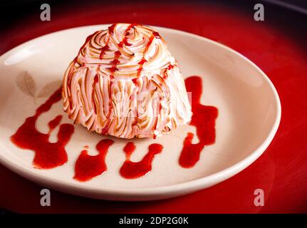 Baked Alaska dessert with browned meringue and raspberry sauce on a red surface; copy space Stock Photo