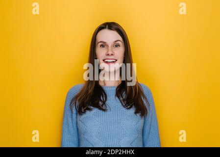 Overjoyed glad young woman with happy face keeps mouth wide opened laughs at something joyfully doesn't hide emotions grins from happiness, wears blue Stock Photo