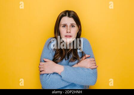 Young brunette woman freezes in light clothing warms up by hugging herself, seasonal changes low temperature heating problem, chills feeling of coldne Stock Photo