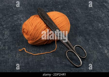 Old rusty tailor scissors and a tangle of orange color woolen yarn in close-up Stock Photo