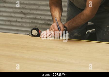 Hand of carpenter lining wooden surface using pencil and tape measure. Stock Photo