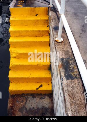 Yellow-painted concrete steps at a berth in the harbour, Greece Stock Photo