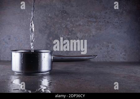 Water pouring into a stainless steel saucepan. Stock Photo