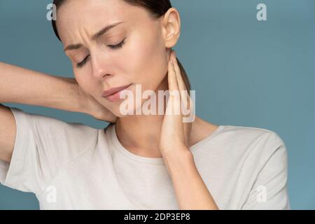 Woman suffering from chronic neck pain, gently massages with hands, feeling tired after long hours work in incorrect posture, closed eyes. Exhausted f Stock Photo