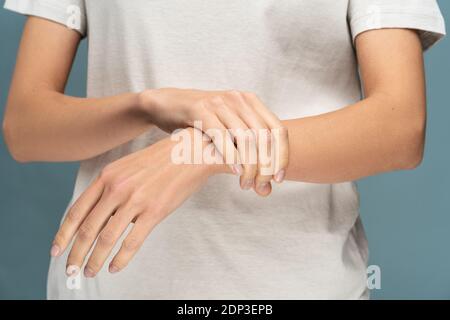 Closeup of woman arms holding her painful wrist caused by prolonged work on computer, laptop, standing over studio blue background. Carpal tunnel synd Stock Photo