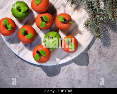 Marzipan sponge apples, green and red. Flat lay on marble board with fir twigs, winter decorations. Stock Photo