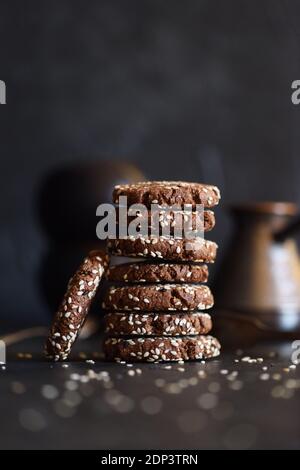 Vegetarian gluten free dessert. Homemade chocolate cookies with sesame seeds in pile on black background copy space front view Stock Photo