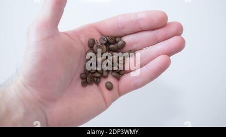 Fragrant roasted coffee beans.  Coffee beans in a man’s hand,in the palm of a coffee,close-up,top view.On a white background, isolation. Stock Photo