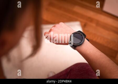 Young caucasian woman looking at the sport watch while doing exercises at home Stock Photo