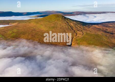 Aerial view of a mountain peak rising above a sea of low cloud and fog in the valley below (Sugar Loaf, Brecon Beacons, Wales)