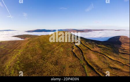 Panoramic aerial view of a mountain summit rising above a sea of low cloud and fog (Sugar Loaf, Wales).