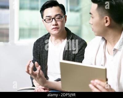 two young asian entrepreneurs discussing business in office using digital tablet Stock Photo