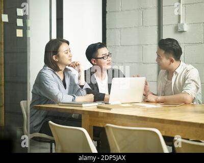 three young asian entrepreneurs meeting in office discussing business using laptop computer