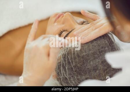 Young woman getting manual relaxing facial massage from hands of masseur Stock Photo