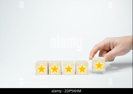 Wood cubes with gold star signs. Man Hand putting wooden five star shape on white background. Best Excellent Services Rating customer experience conce Stock Photo