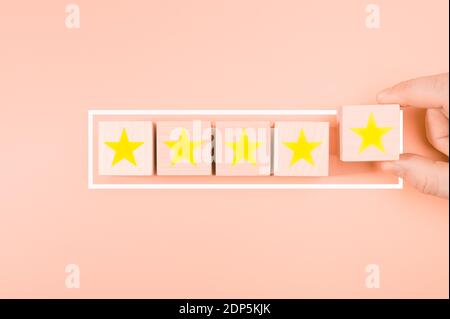 Concept excellent rated services. Hand putting Wood block cube gold five star shape on wooden table pink background. Wooden 5 stars. Concept excellent Stock Photo