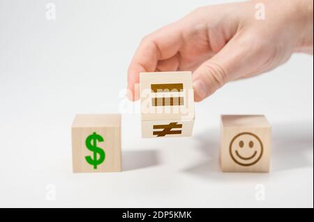 Happiness or money as a choice in life. Hand flip wooden cube with symbol unequal change to equal sign. white background. equality concept on wooden c Stock Photo