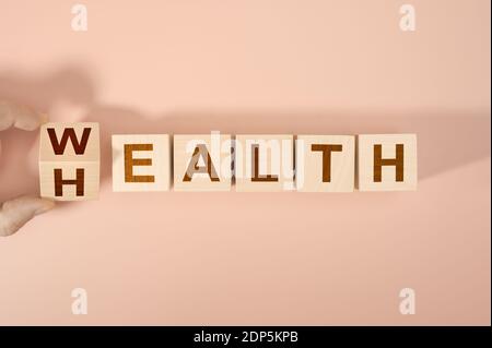 Hand is turning a dice and changes the word Health to Wealth. Wooden blocks with the word Health and Wealth. Concept of choosing priority in life and Stock Photo