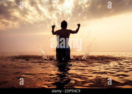 Toned Photo of Happy Man Silhouette with splashes in the Water on the Sunset Background Stock Photo