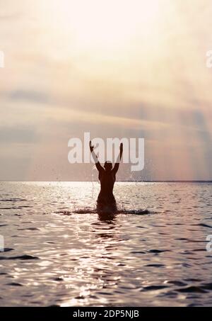 Toned Photo of Happy Young Man Silhouette with Hands Up in the Water Stock Photo