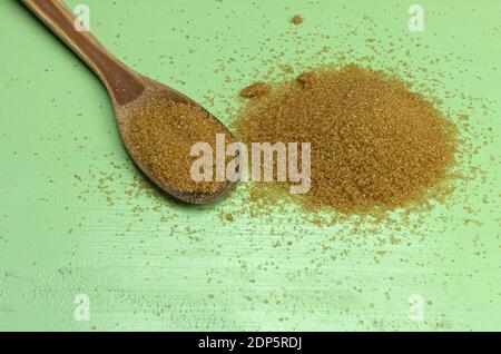 A pile of brown cane sugar and a wooden spoon on green background Stock Photo