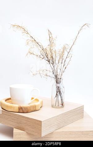 Pampas grass in glass vase on wooden table near white wall Stock Photo