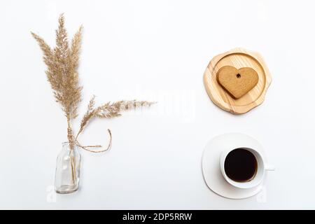 Minimalistic flat lay with pampas grass, cup of coffee and heart shaped gingerbread cookies on white table with place for text. Stock Photo