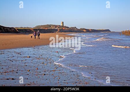 Two people dog walking on the beach at low water on a fine winter day in North Norfolk at Happisburgh, Norfolk, England, United Kingdom. Stock Photo