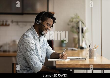 Smiling biracial man watch webinar on laptop make notes Stock Photo